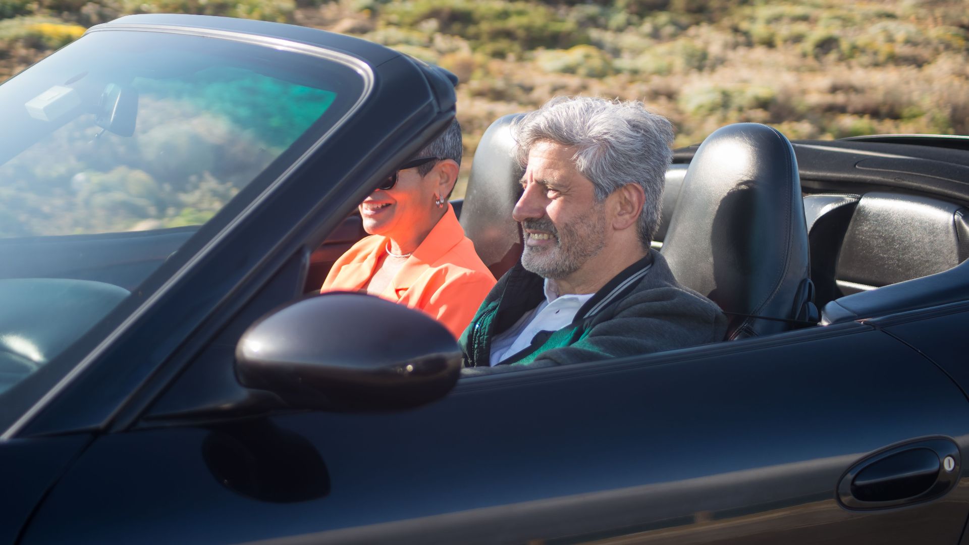 Happy senior couple driving a luxury convertible car on a sunny day outdoors in Portugal.