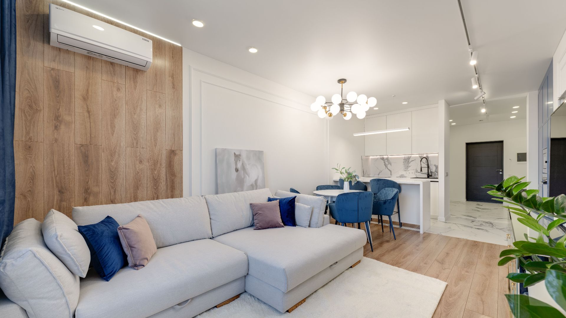 Contemporary living room with stylish furniture, elegant chandelier, and open kitchenette.