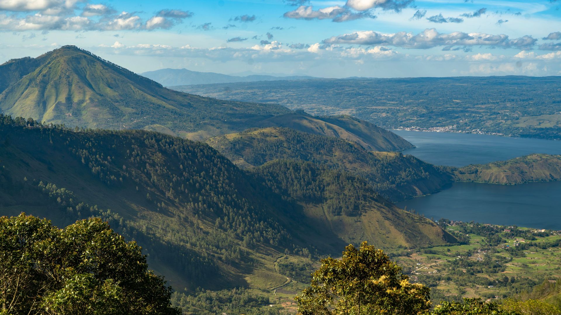 A breathtaking aerial view of Lake Toba in Sumatra, surrounded by lush mountain landscapes under a vibrant sky.