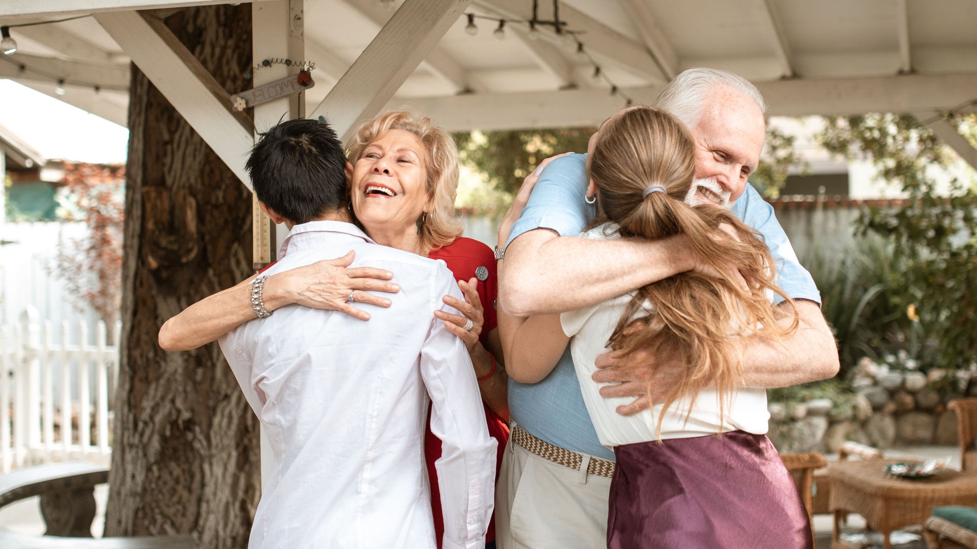 A joyful family reunion outdoors with warm hugs and smiles under a wooden pergola.