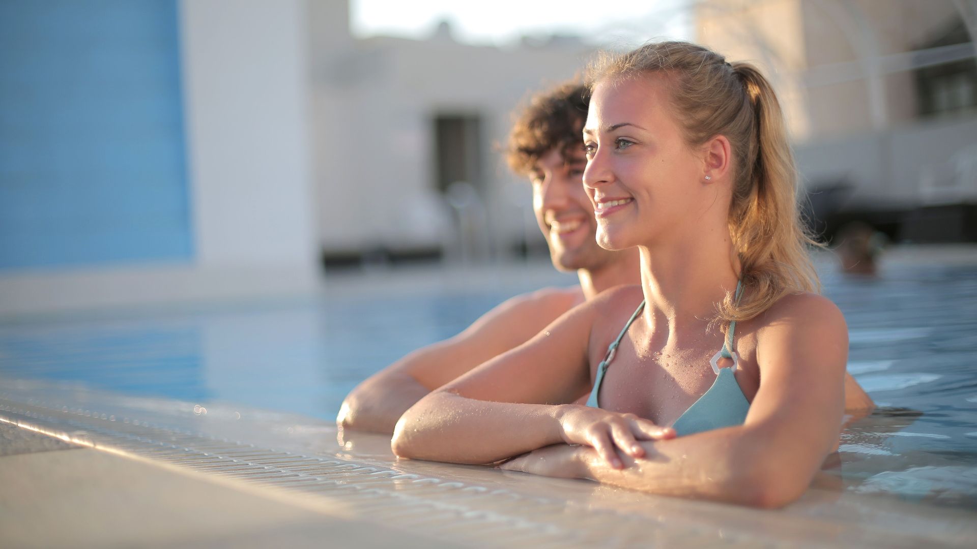 Smiling young friends in swimsuit chilling together on poolside and looking away enjoying summer holidays in resort