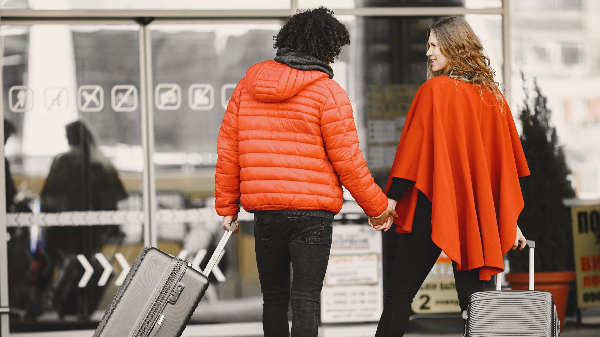 A couple holding hands with luggage, entering an airport for a travel journey.