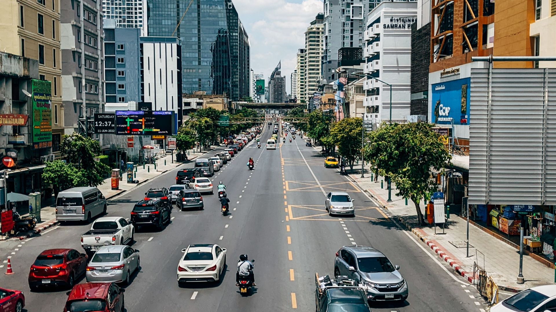 A vibrant city scene depicting busy urban traffic amidst towering skyscrapers under a bright sky.