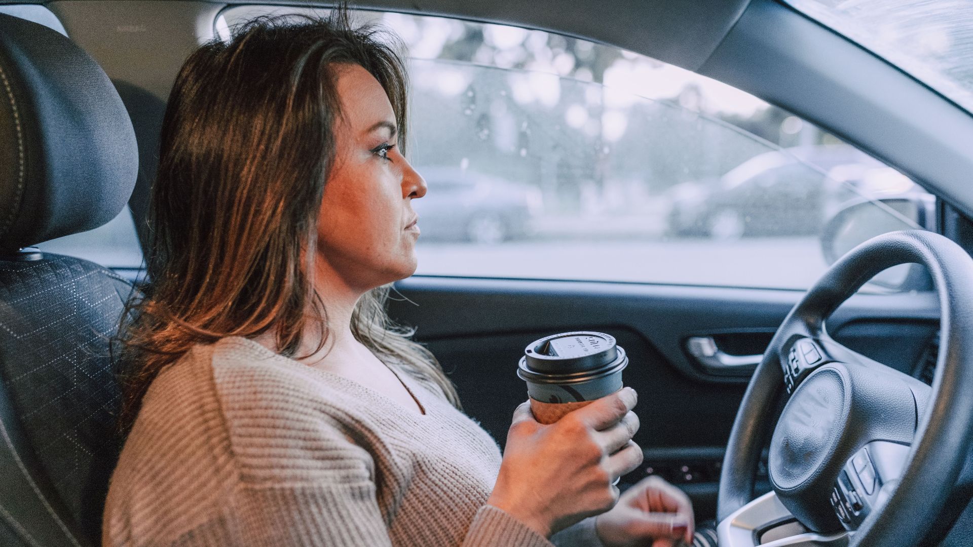 A woman in a car holding a disposable coffee cup, showing focus.