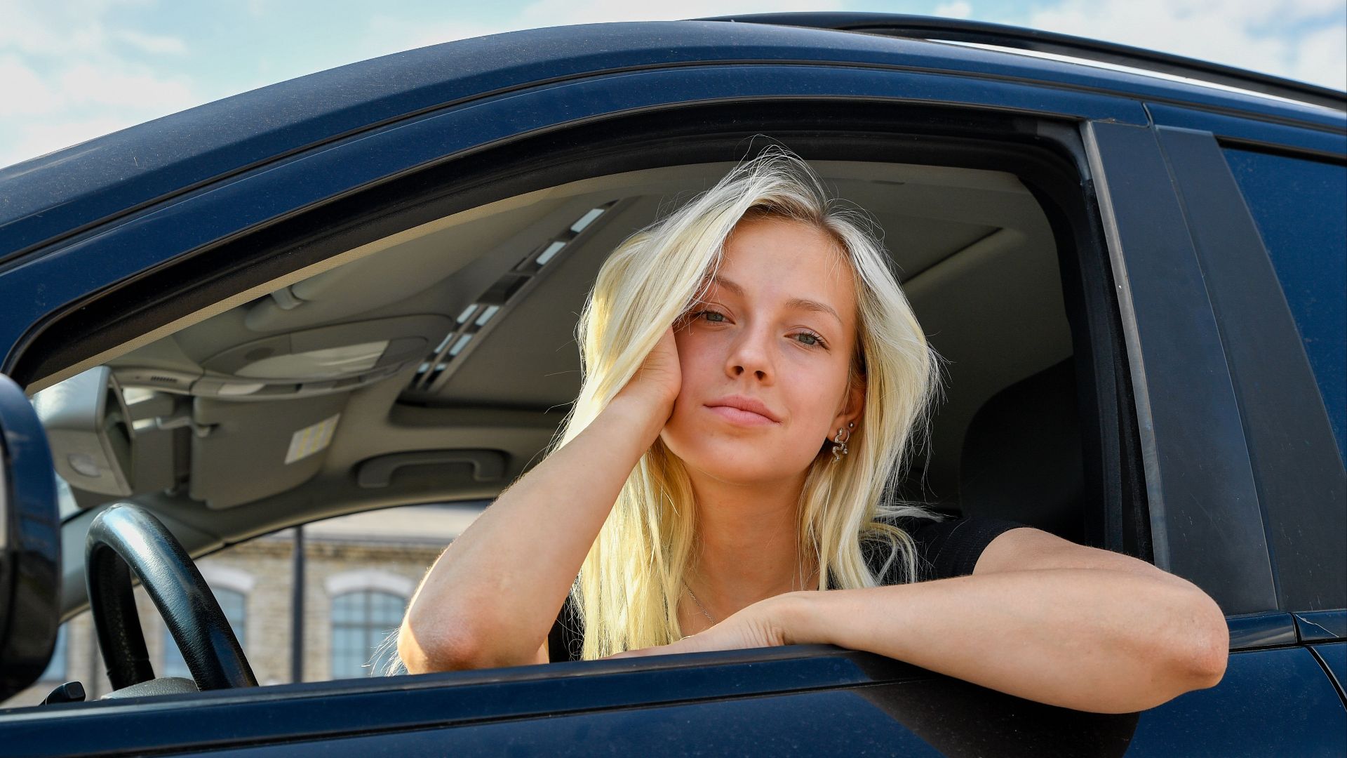 A trendy young woman gazes thoughtfully out of a car window under the summer sunlight.