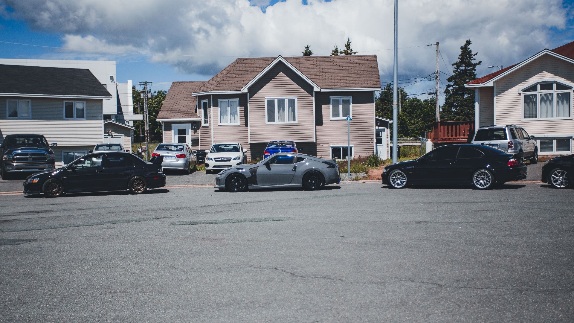 Sunny neighborhood street with modern homes and parked vehicles on a bright day.