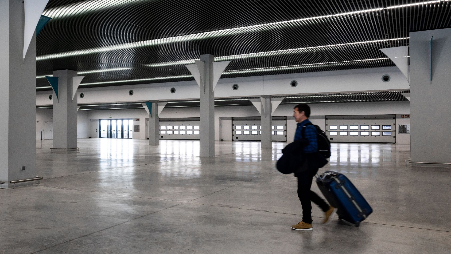 A man with luggage walking through a spacious, modern, empty airport hall.