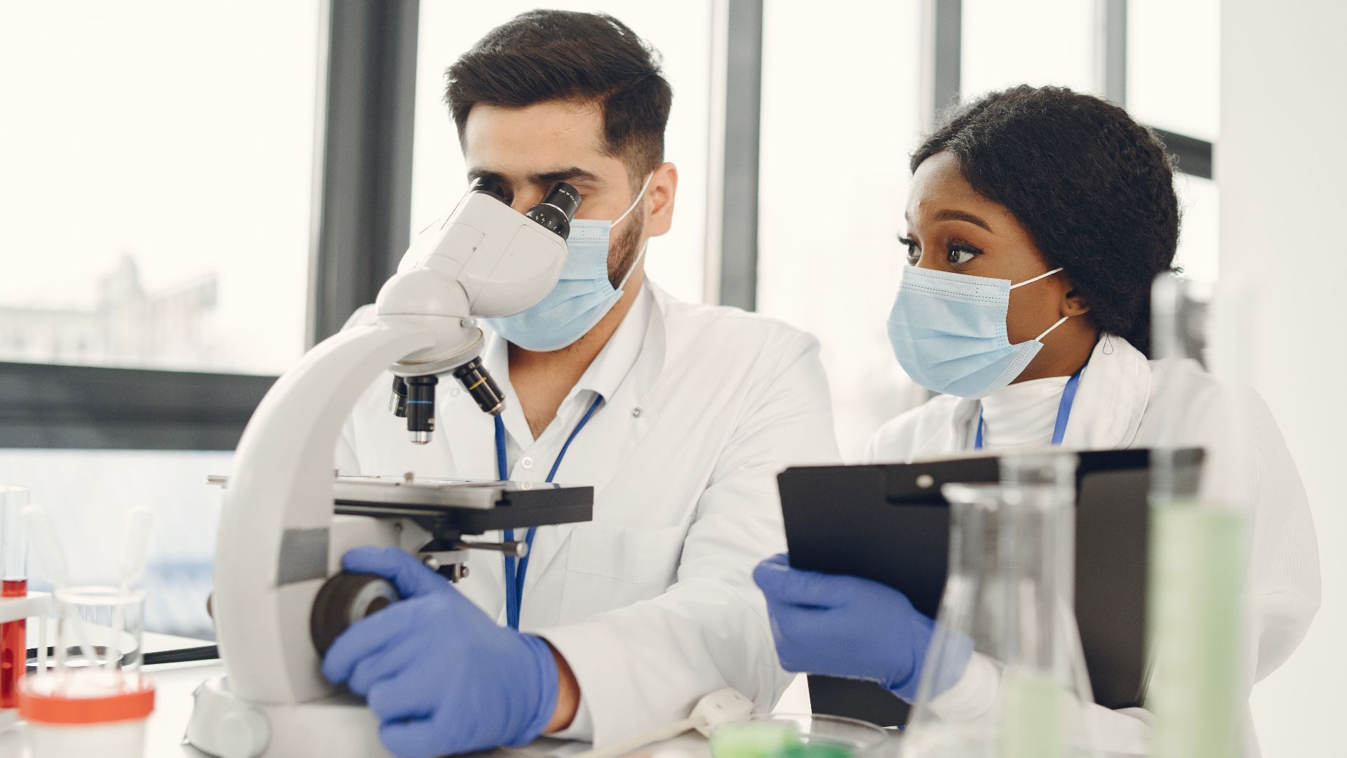 Researchers using a microscope and taking notes in a modern lab.