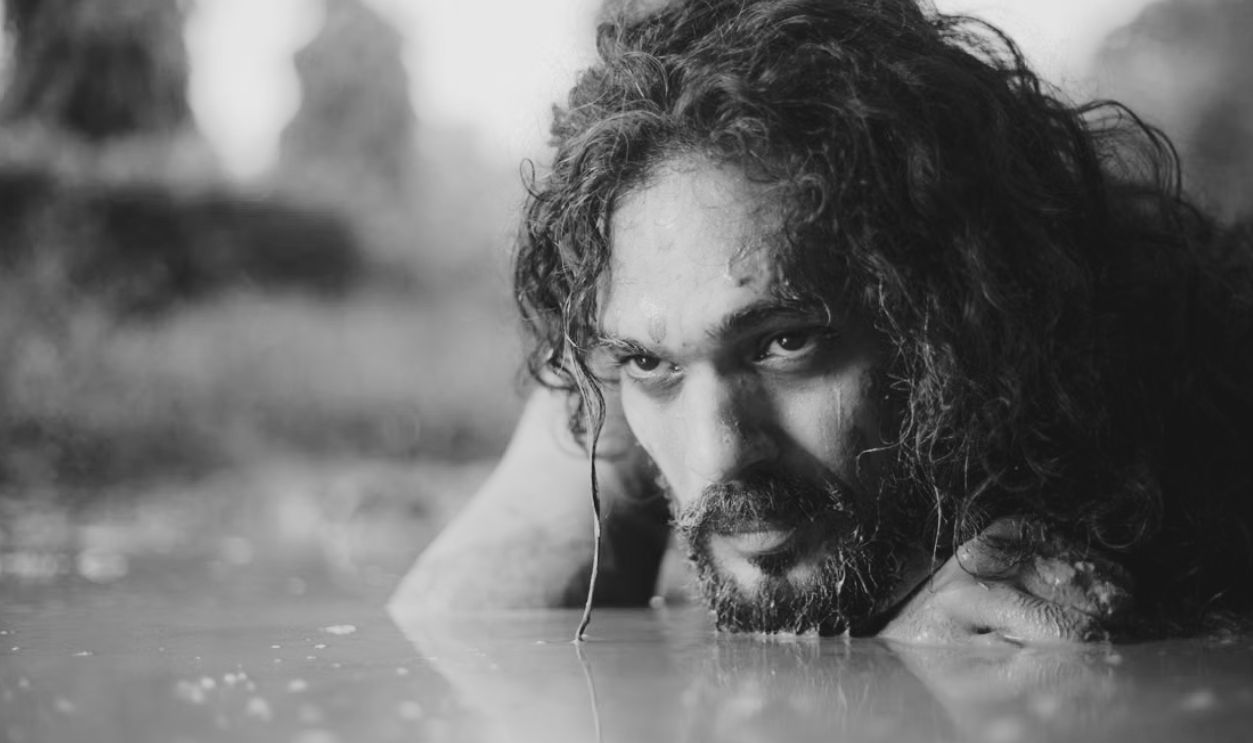 Portrait of a man with long hair and beard submerged in muddy water, highlighting intense focus
