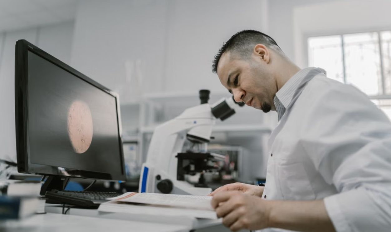 Asian man reading in a laboratory, surrounded by equipment and microscope, focused on work