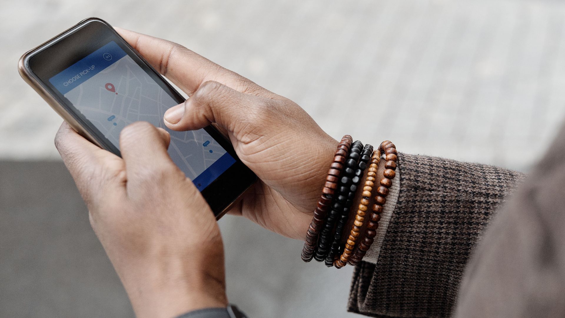 Close-up of hands with bracelets navigating on smartphone using GPS app outdoors.