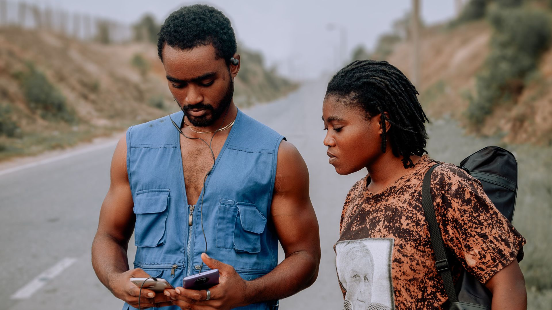 A young couple uses a phone for navigation on a rural road trip.