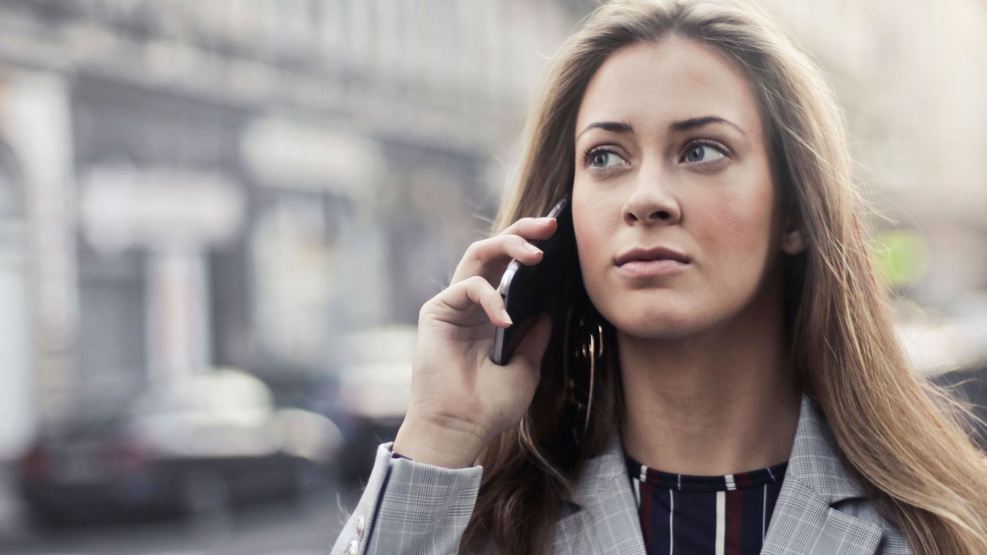 Fashionable young woman talking on smartphone in urban Budapest setting.