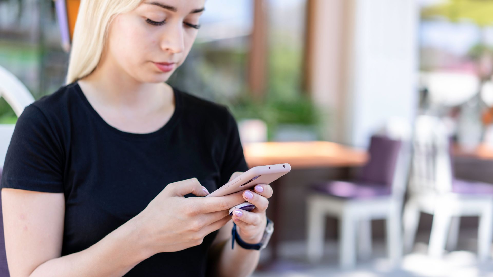 Young woman in a black shirt texting on her smartphone at an outdoor cafe.