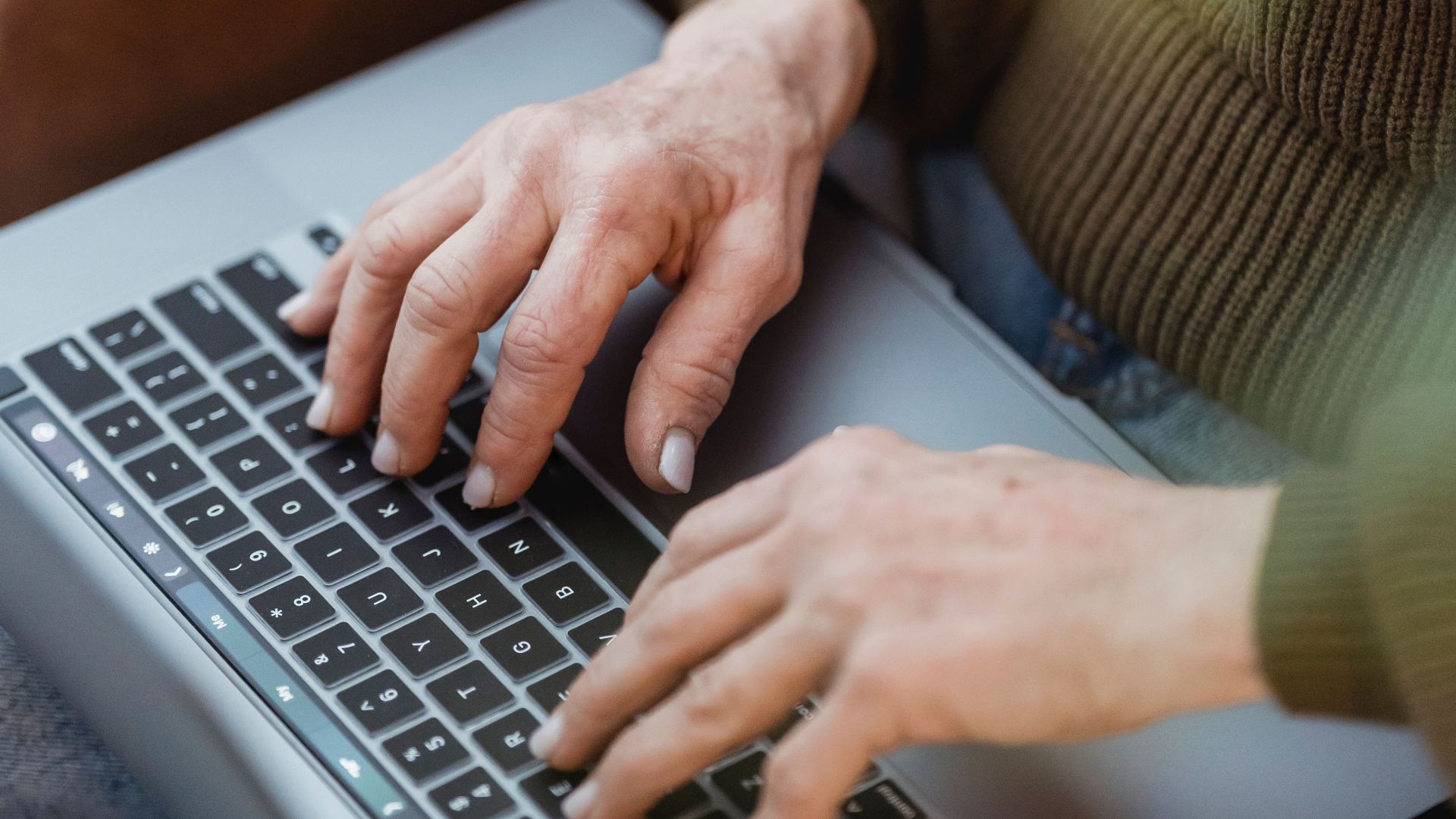 Crop unrecognizable female in casual clothes working on modern netbook keyboard while sitting on cozy armchair