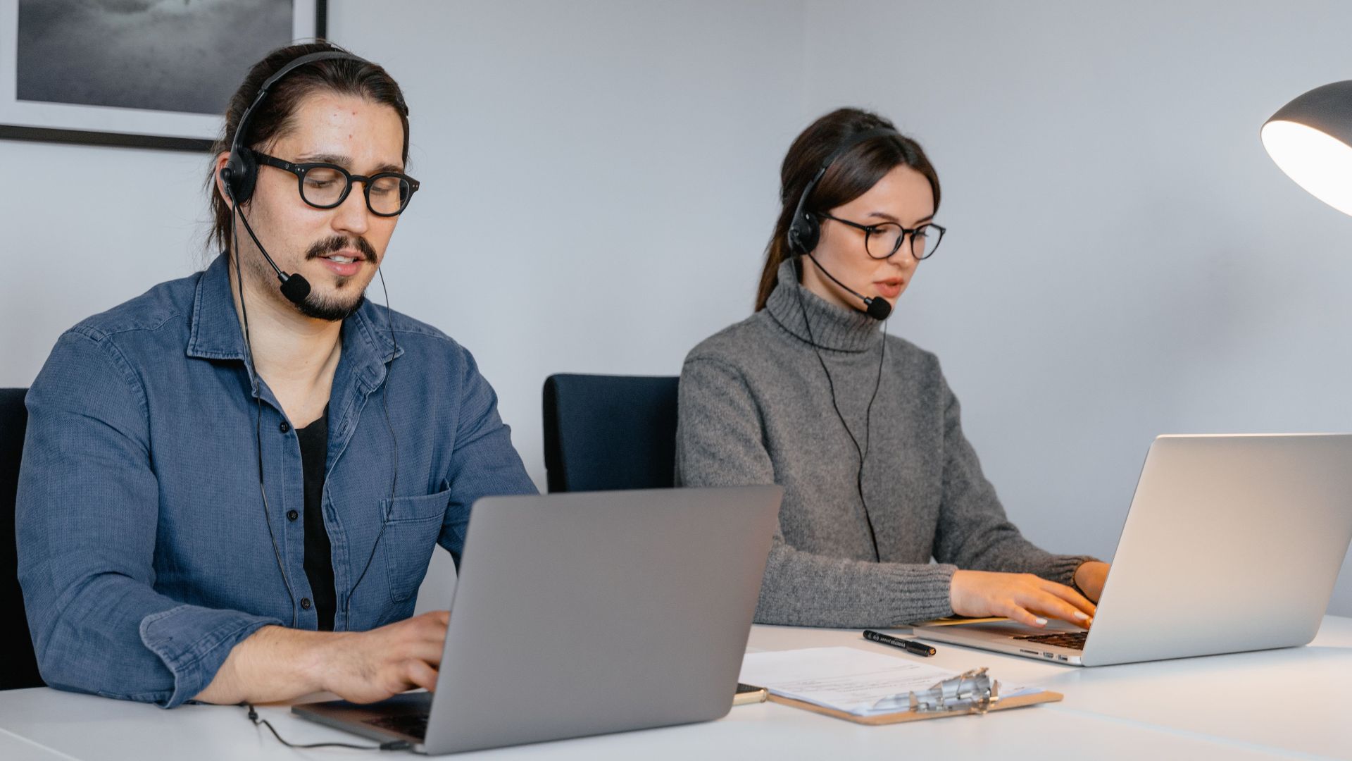 Two focused call center agents working on laptops with headsets in an office setting.