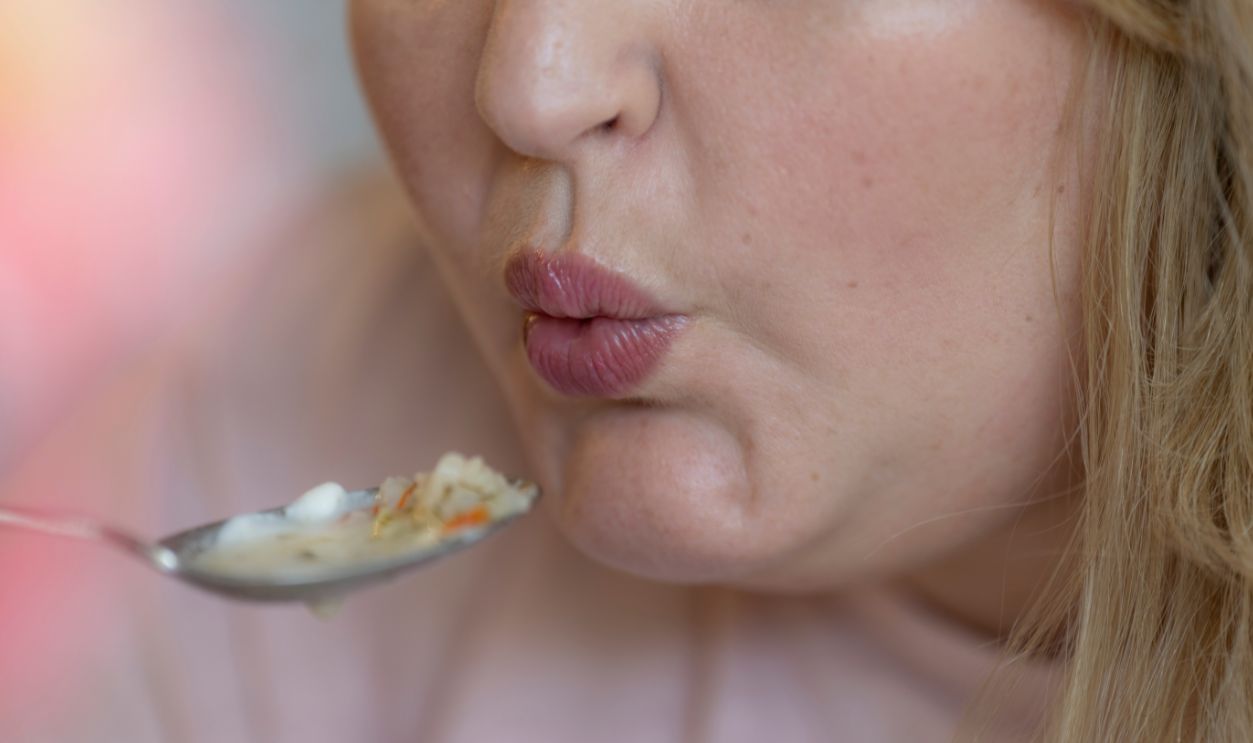 Close-up of a woman blowing on a hot spoonful of soup before eating. The image conveys the warmth and comfort of homemade meals and mindful eating.