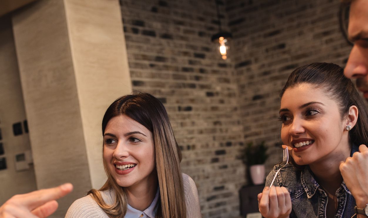 Group of young friends having fun in restaurant, talking and laughing while dining at table.