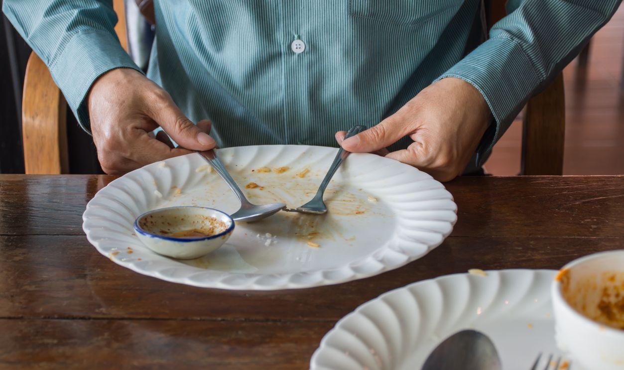 Man holding fork and spoon with empty dirty white plate after eating