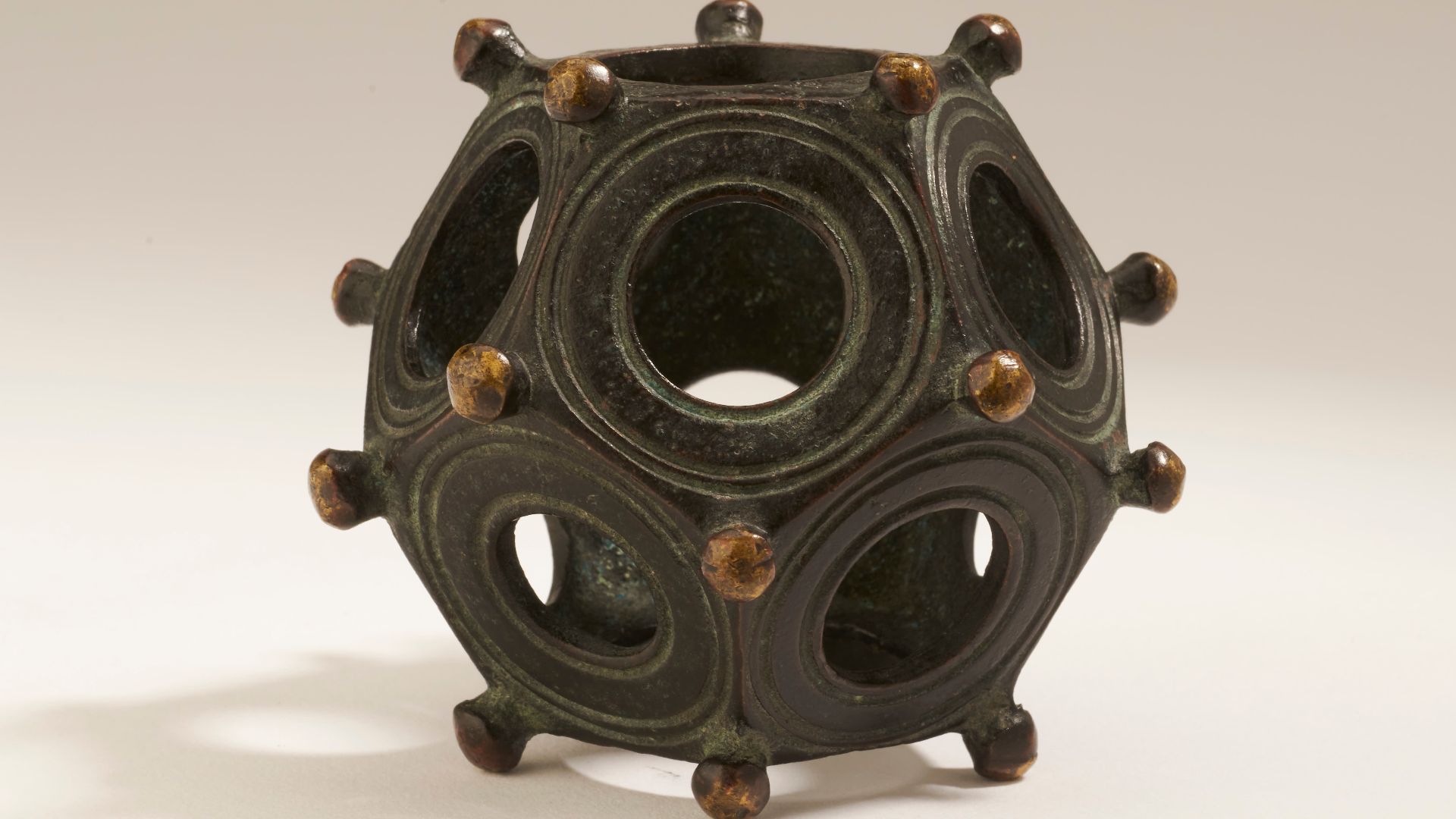 This possibly Gallo-Roman 12-sided bronze object has 12 circular holes of different diameters set within 12 equal pentagons, which are marked by spherical projections of equal size at each corner. Concentric grooves are forged around the holes of each of 
