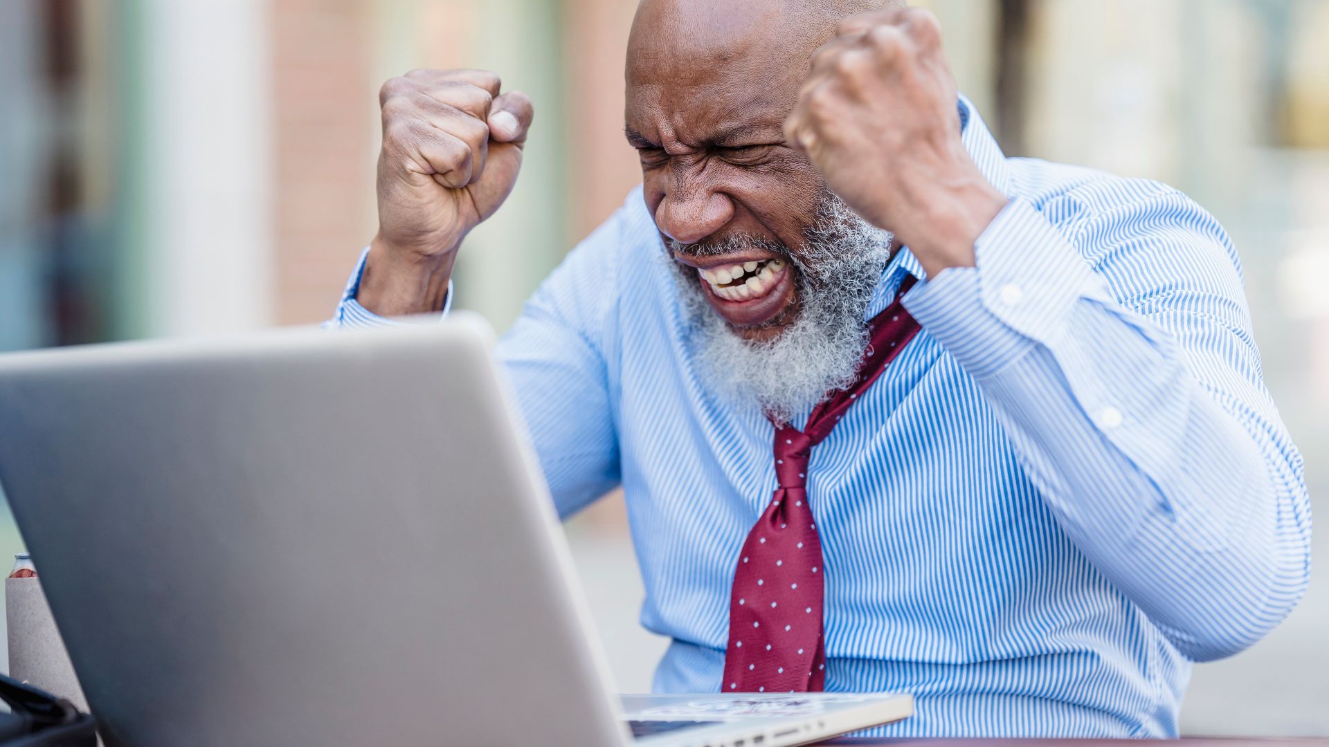 African American businessman showing frustration working on a laptop outdoors.