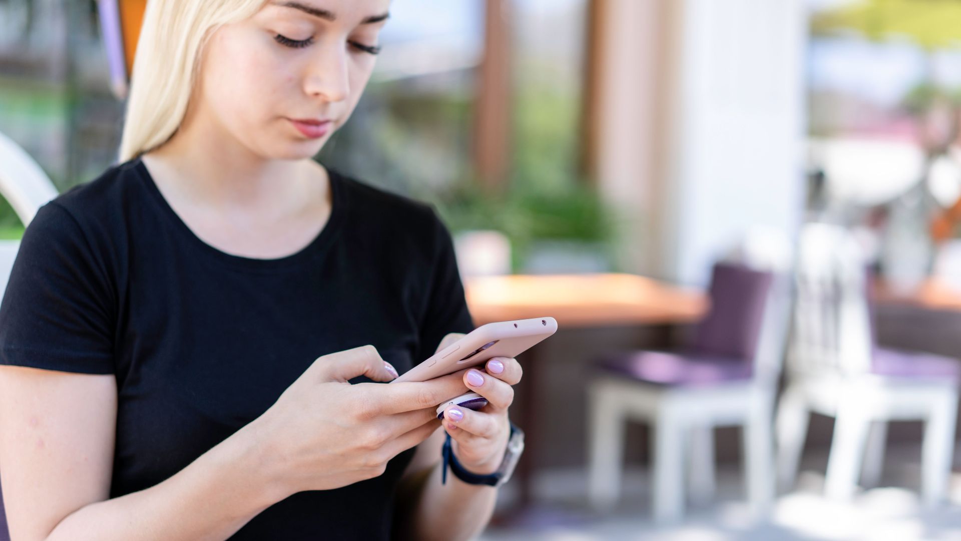 Young woman in a black shirt texting on her smartphone at an outdoor cafe.