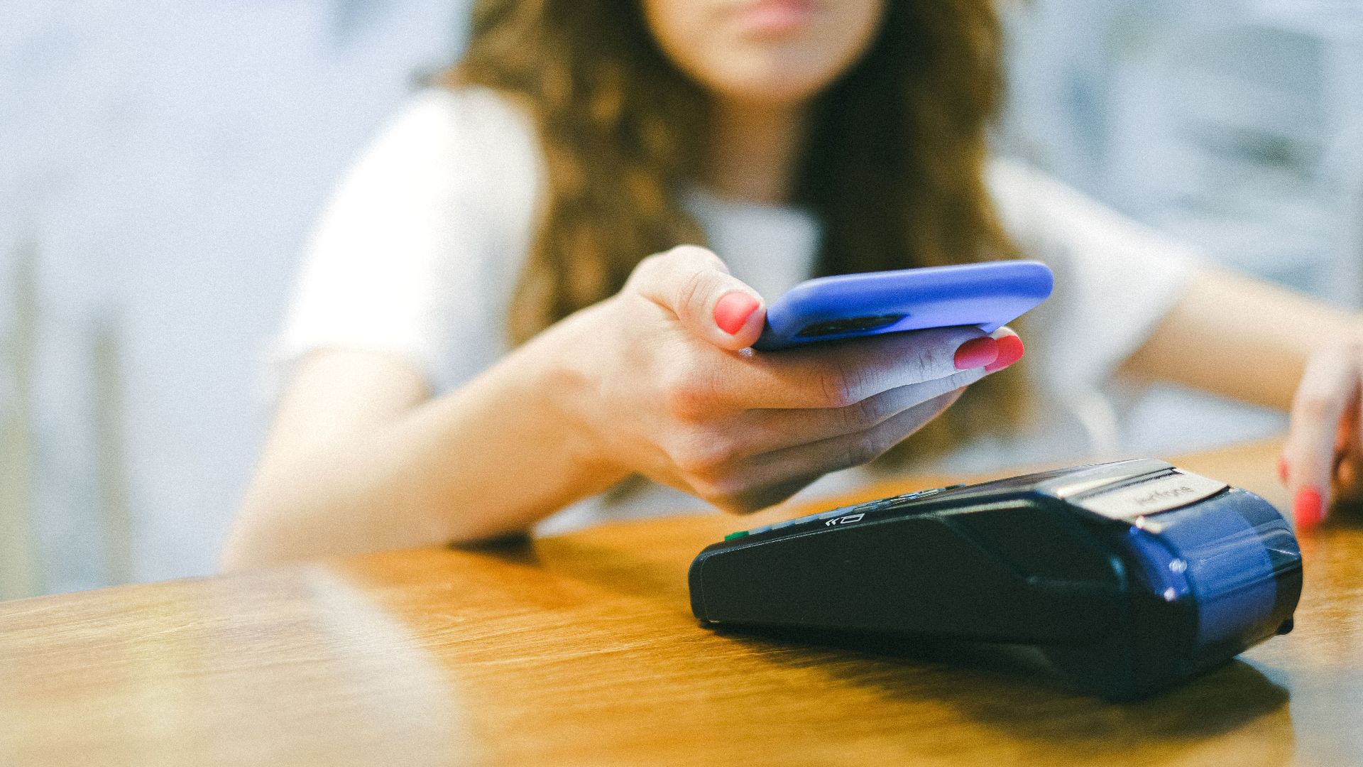 A woman processes a contactless payment using her smartphone at a payment terminal.
