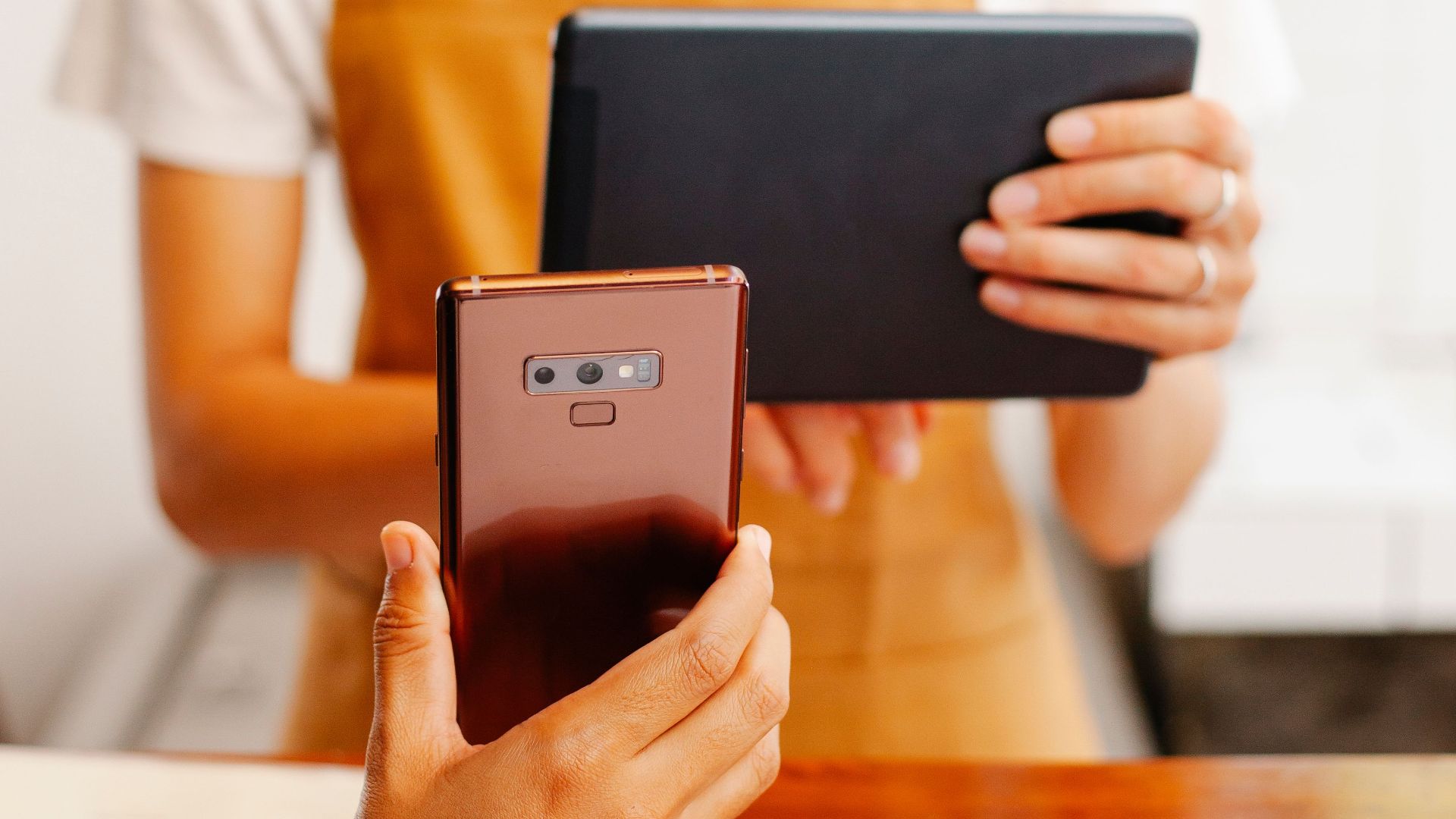 Crop unrecognizable cafeteria employee showing cellphone to female coworker with tablet at counter in daytime