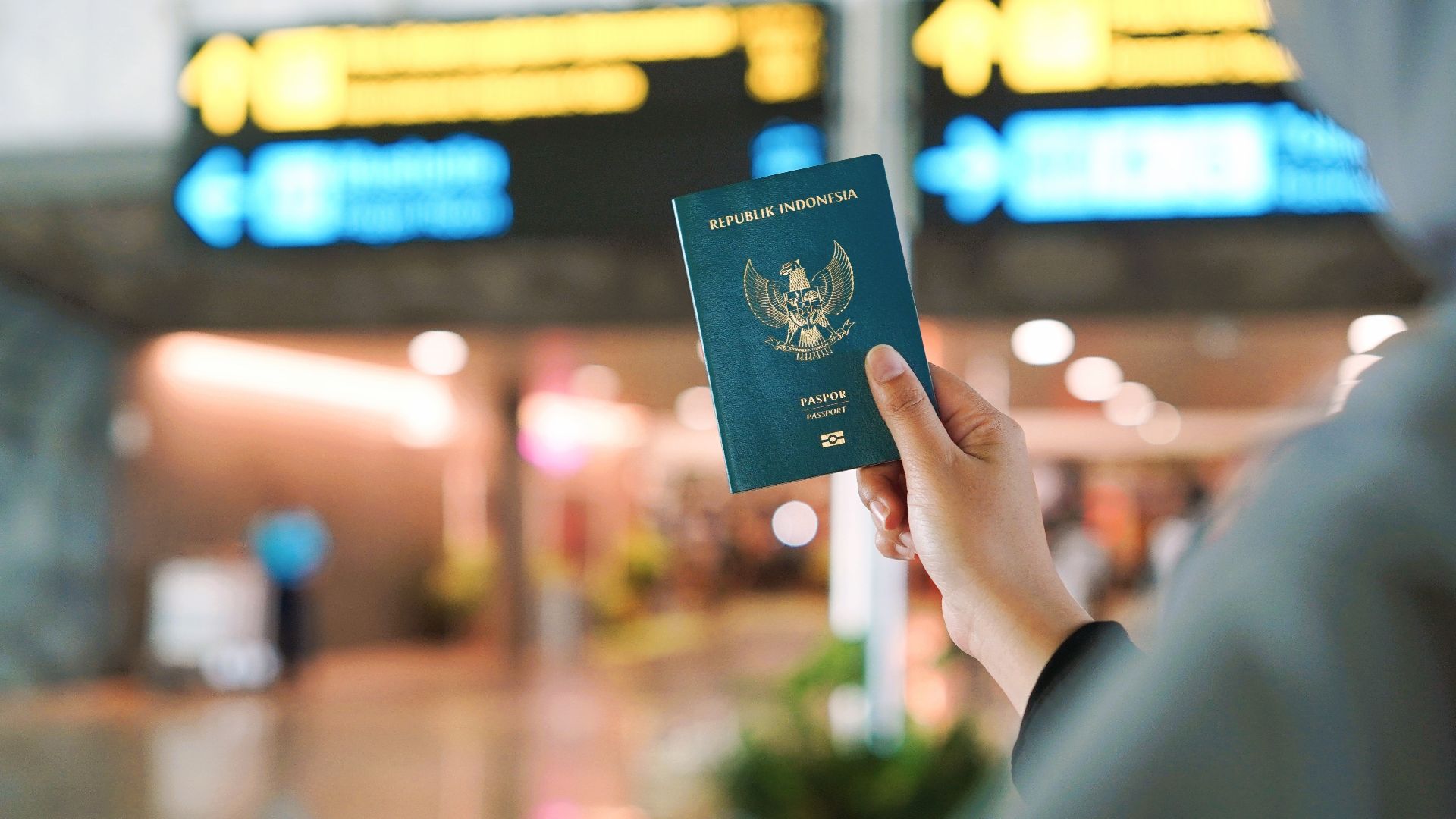 A person holding an Indonesian passport at a busy airport terminal in Yogyakarta, Indonesia.
