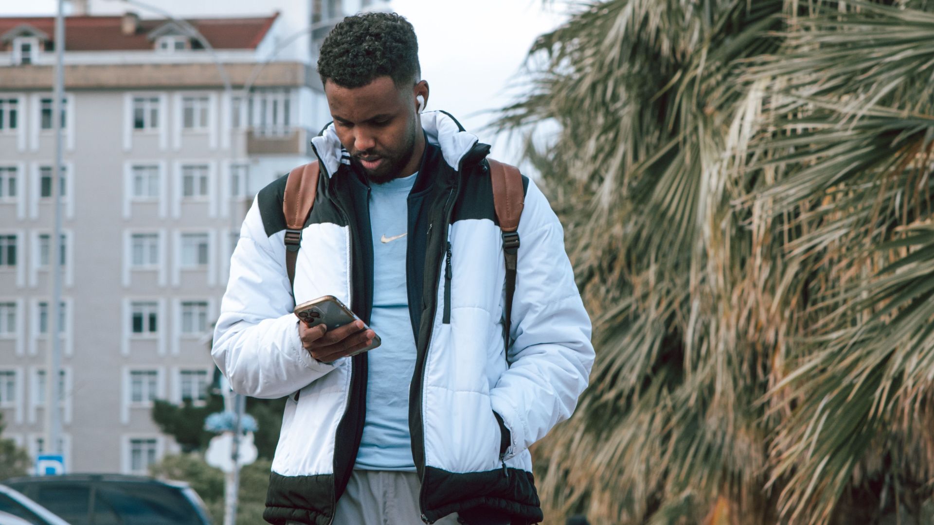 Casual scene of a man texting on a city sidewalk wearing stylish outerwear.