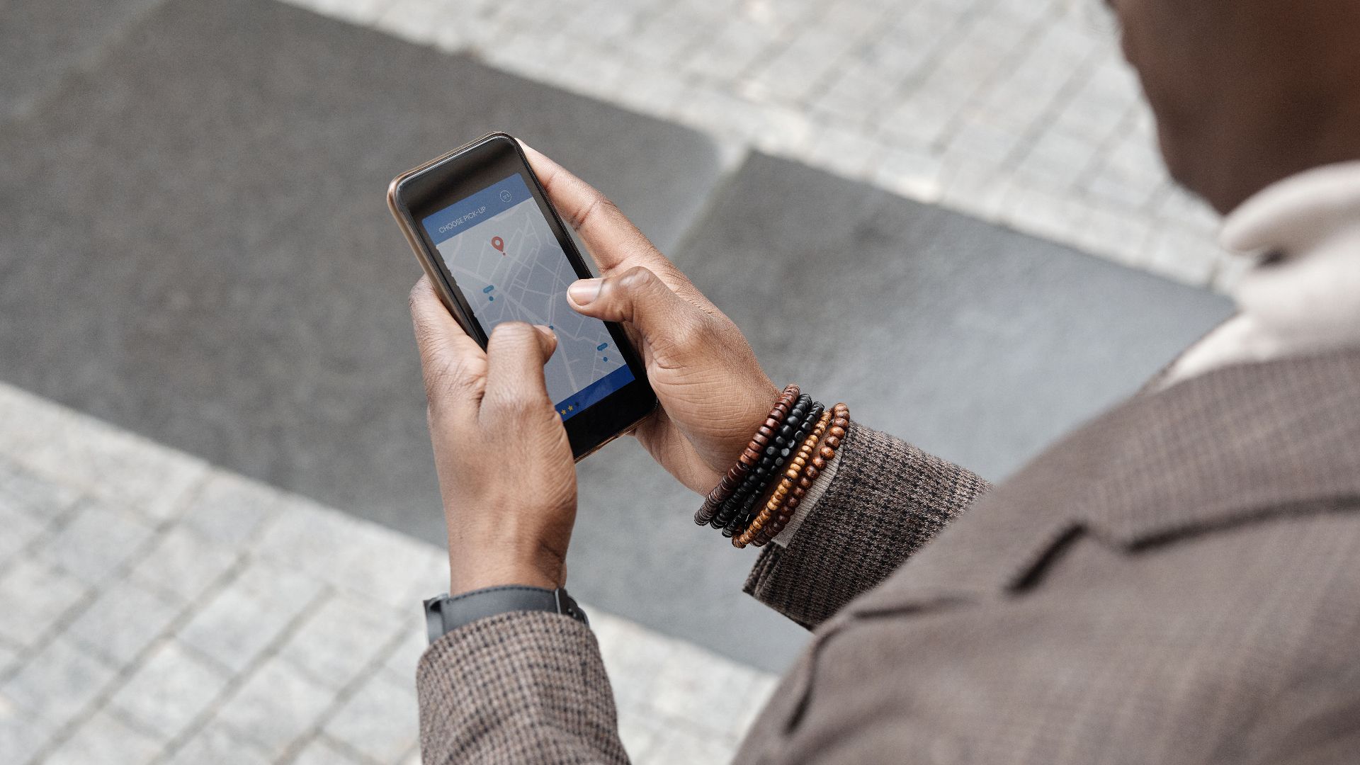 A stylish professional adult using a smartphone with a navigation app on an urban street.