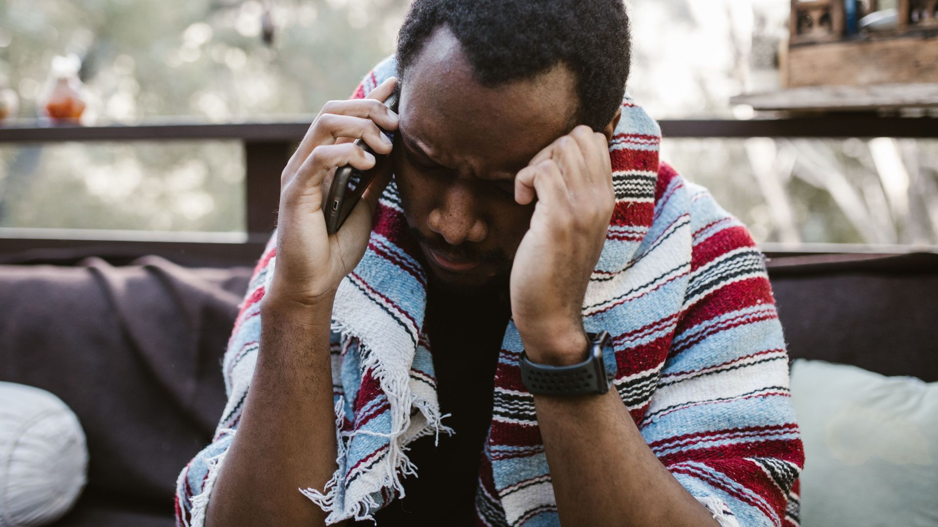 Thoughtful adult man having a conversation on the phone while wrapped in a cozy blanket outdoors.