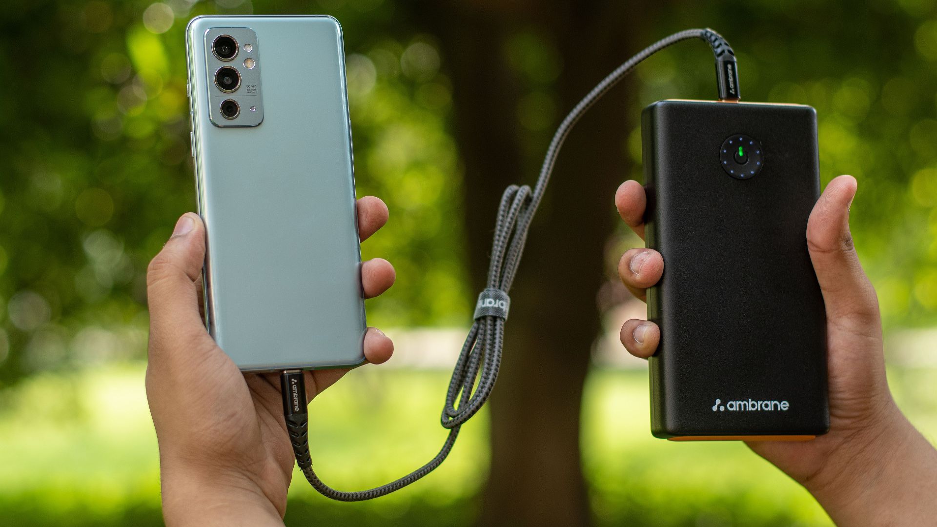 Close-up of hands holding a smartphone connected to a power bank outdoors.