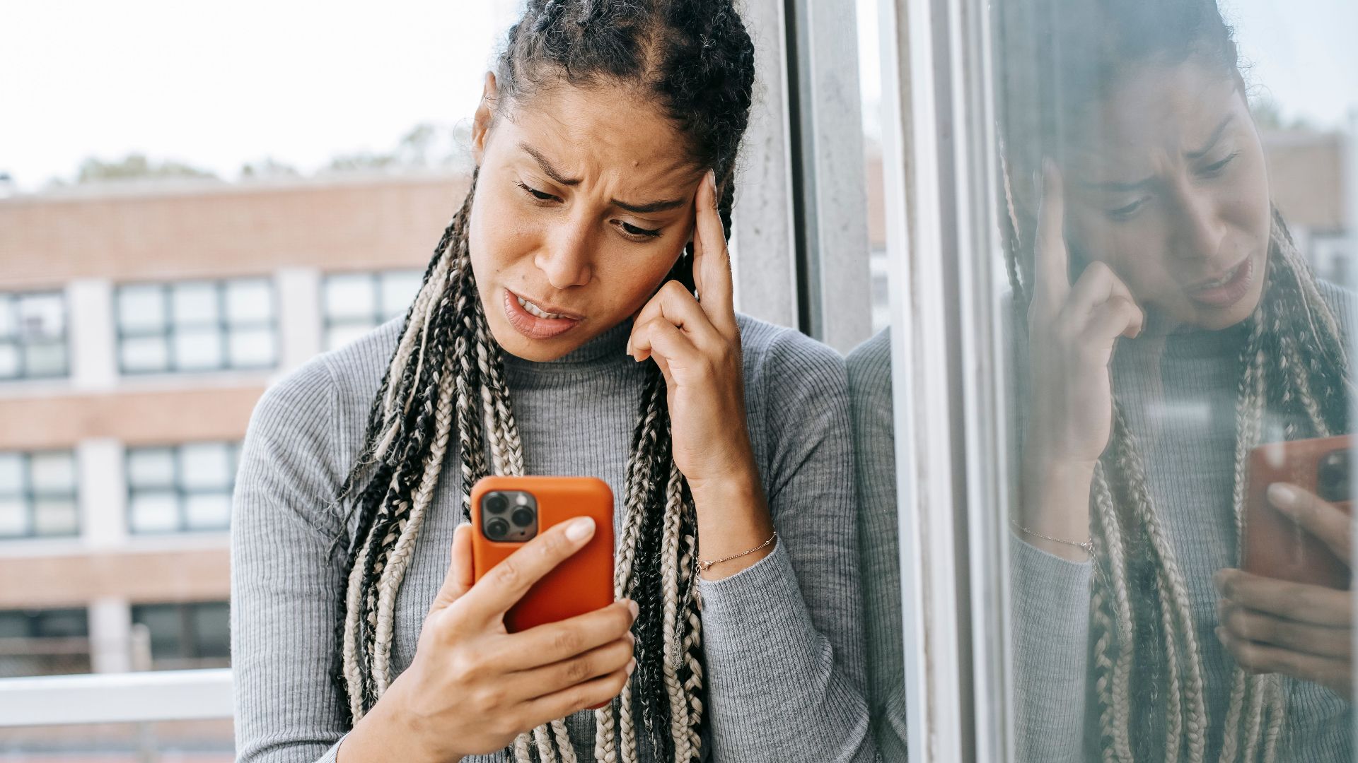 Unhappy African American female standing on balcony while holding smartphone and looking at screen