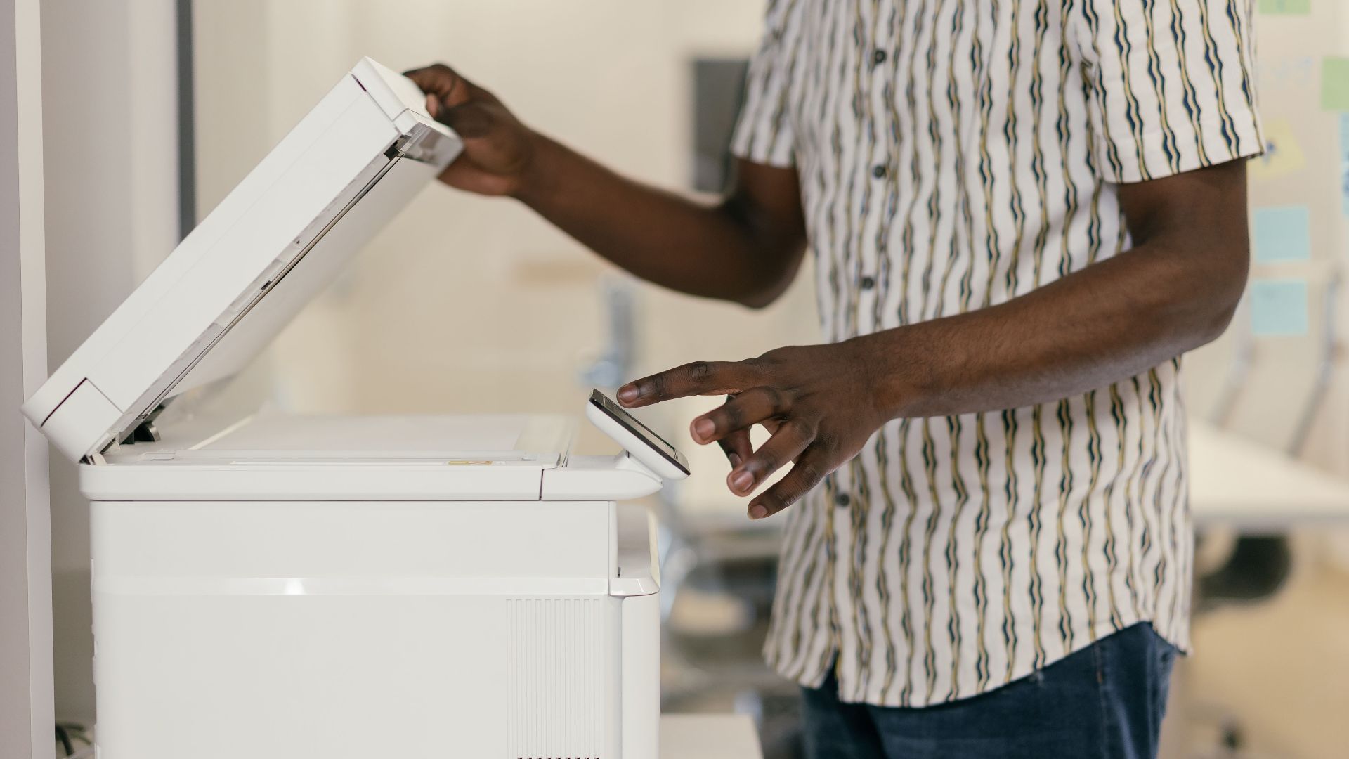 Person operating photocopier in modern office setting, engaging with technology.