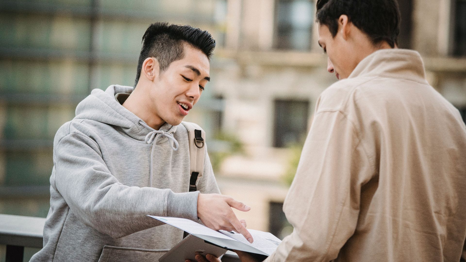 Side view of young multiracial male students in casual wear talking about papers on new project in folder