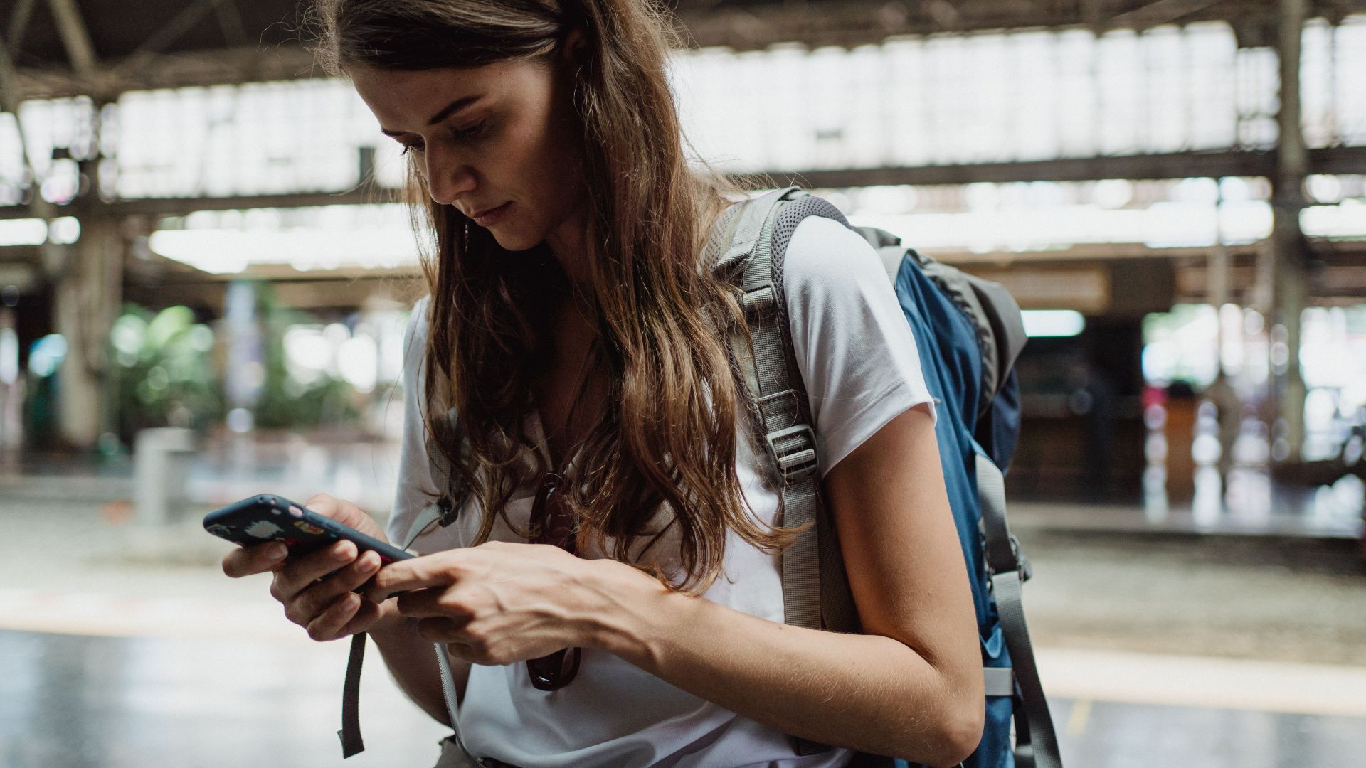 A young woman checks her smartphone while traveling at a train station.