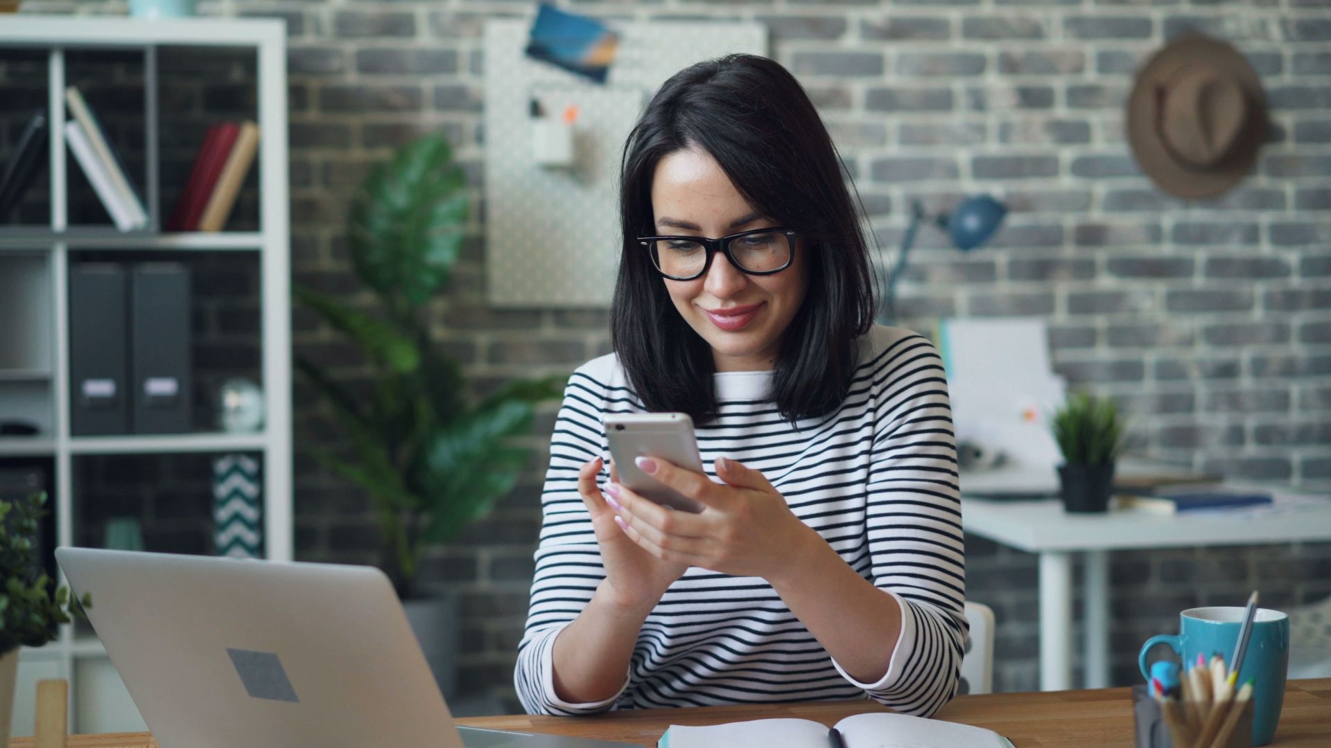 Confident female office worker smiling while checking her smartphone at her desk.