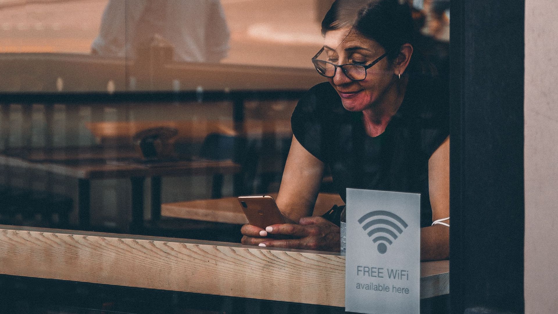 A woman using her smartphone at a cafe window in London, reflecting urban lifestyle.
