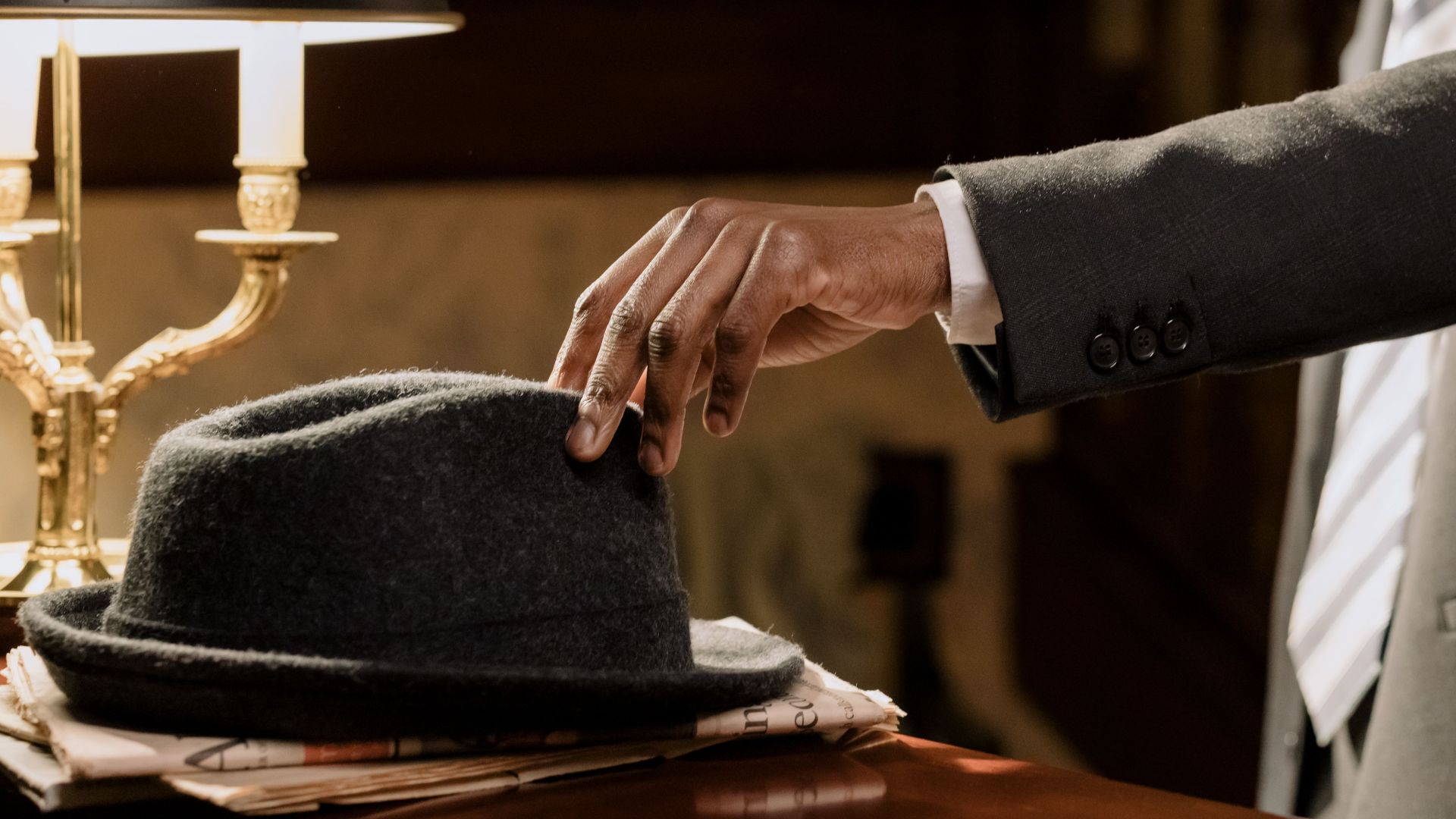 A moody noir detective scene with a man reaching for a fedora under warm lighting.
