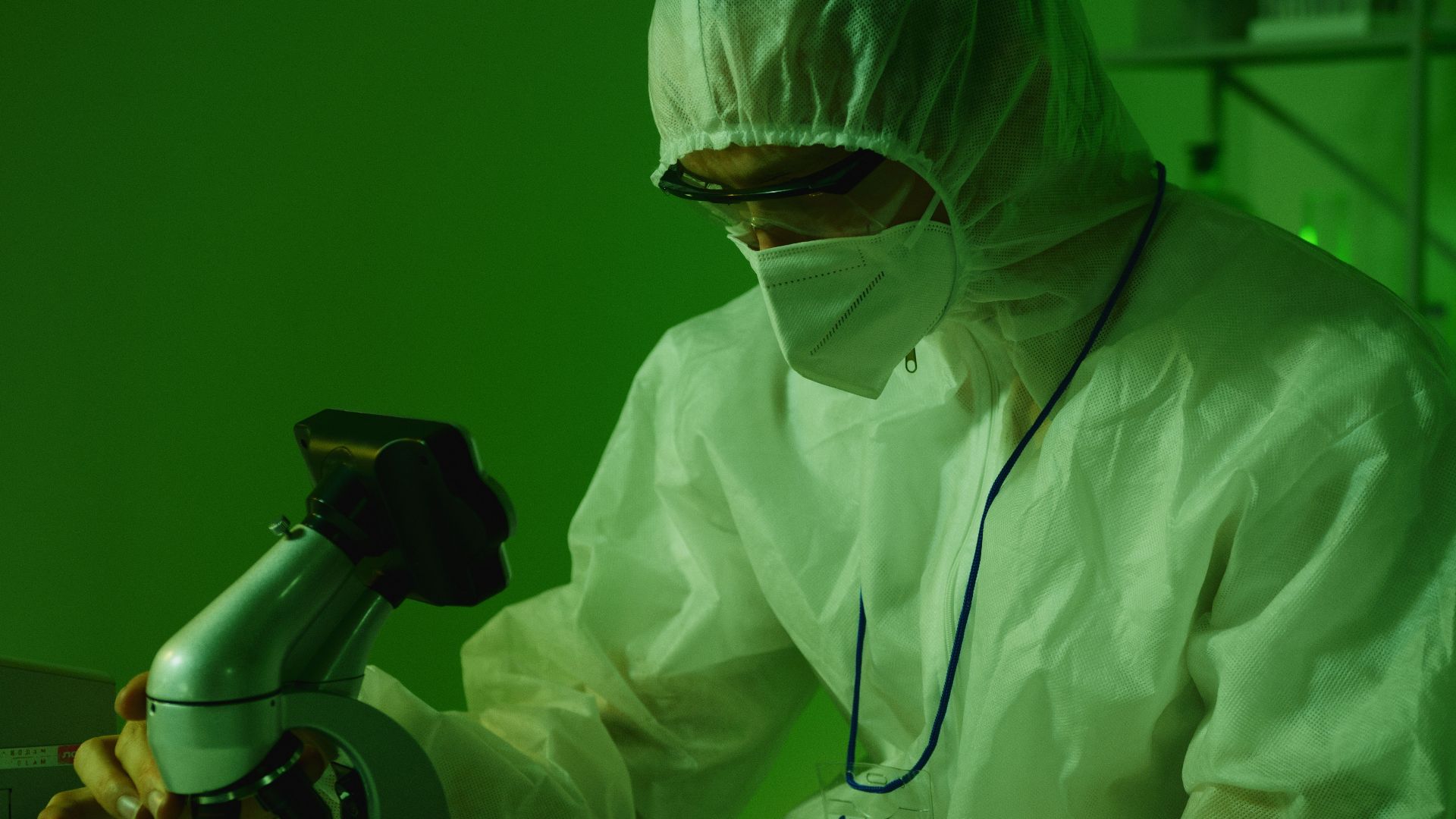 Medical professional in protective gear using a microscope in a laboratory setting.