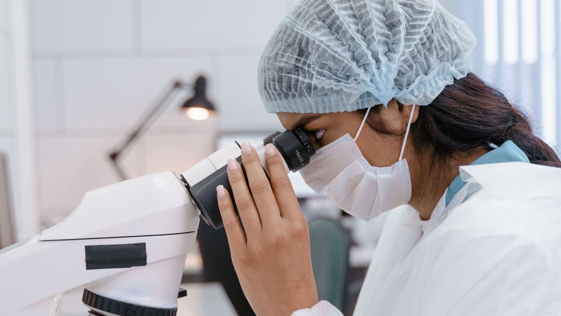 Female scientist in lab coat using microscope for research in a laboratory setting.