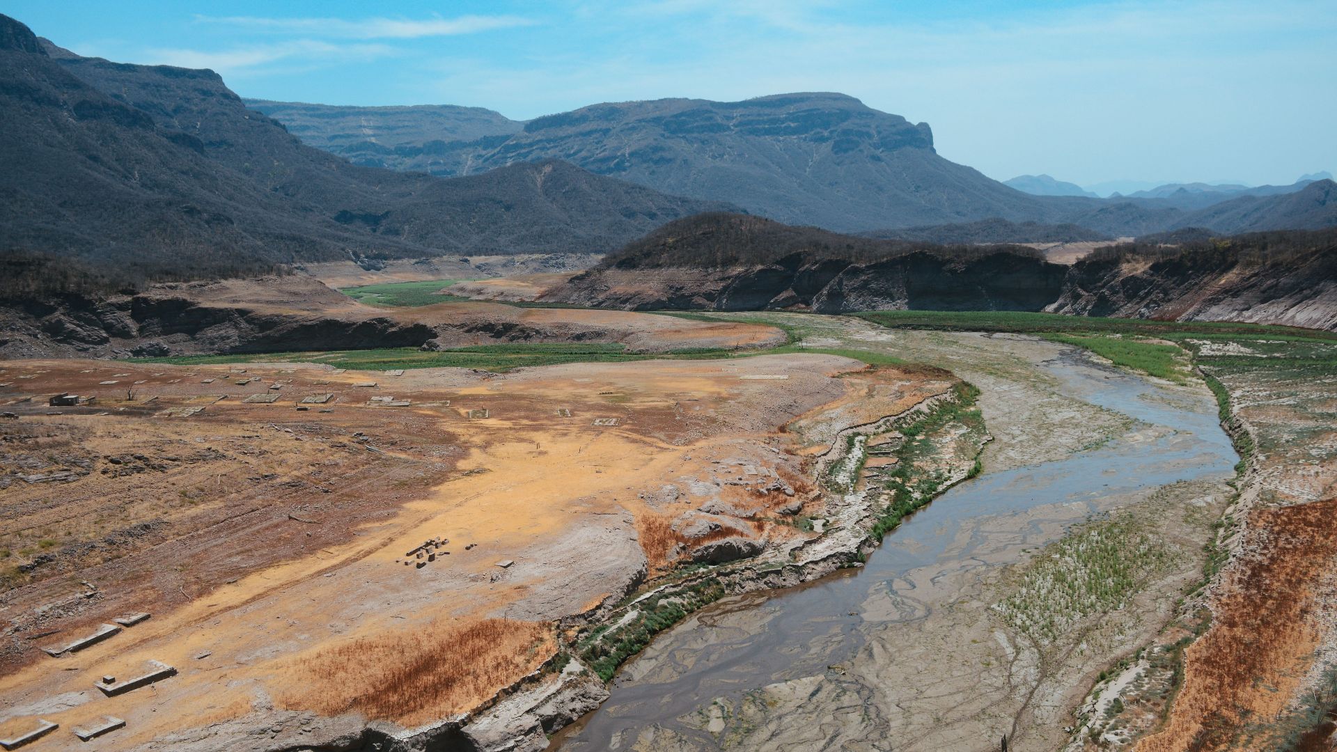 Aerial view of barren hills and a meandering river in Chihuahua, Mexico, under a clear blue sky.