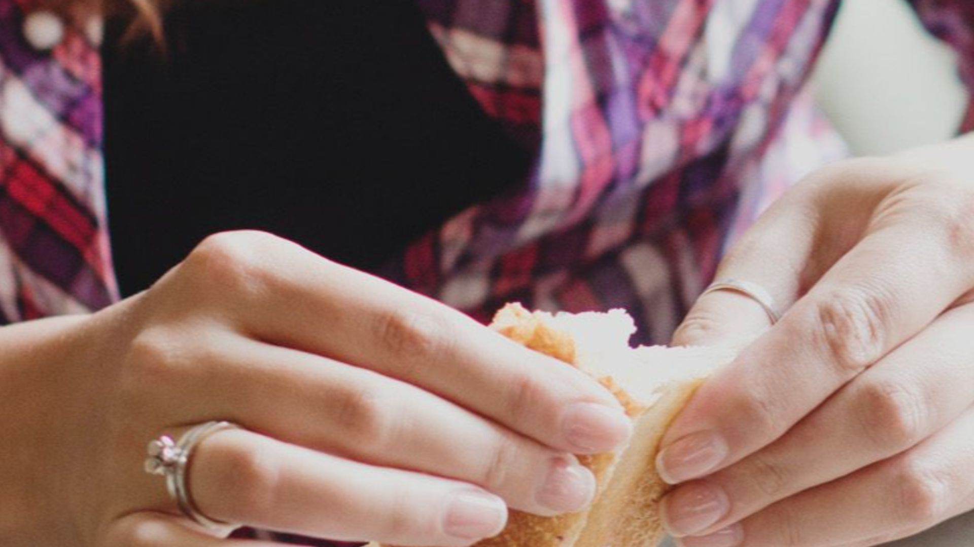 From above female wearing casual clothes sitting at table in restaurant and eating tasty sandwich with coffee while enjoying weekend