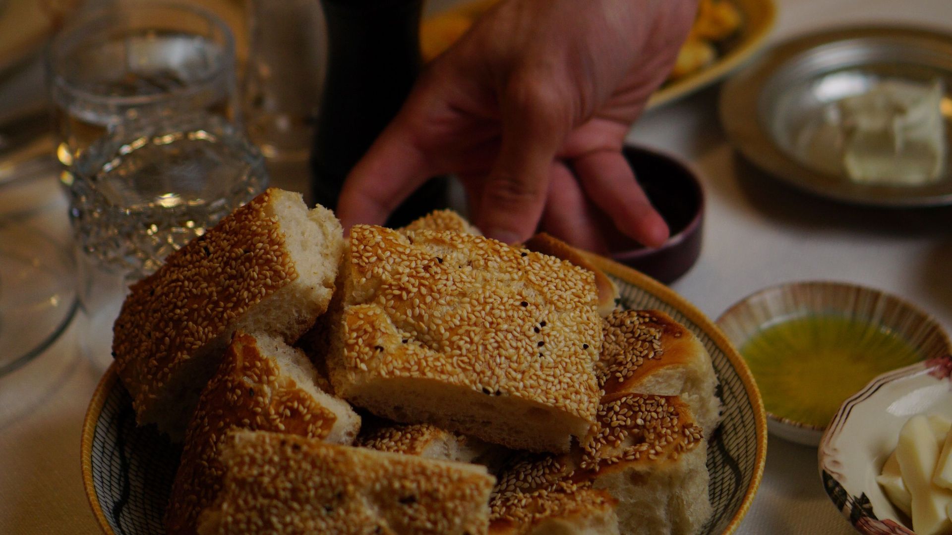Hand reaching for traditional Turkish bread on a table filled with diverse dishes.