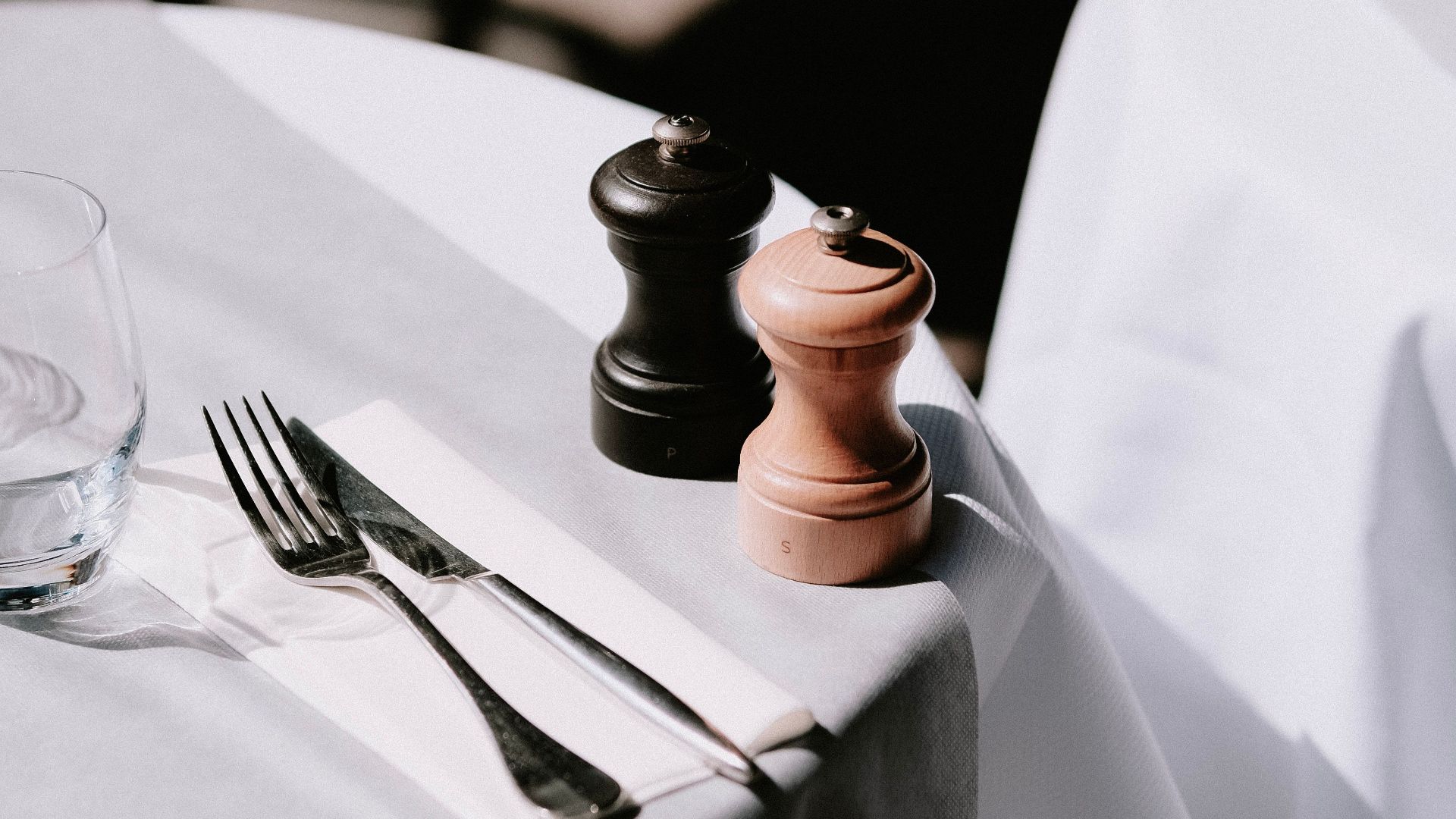 Minimalistic table setting featuring cutlery and pepper mills on a sunlit table.