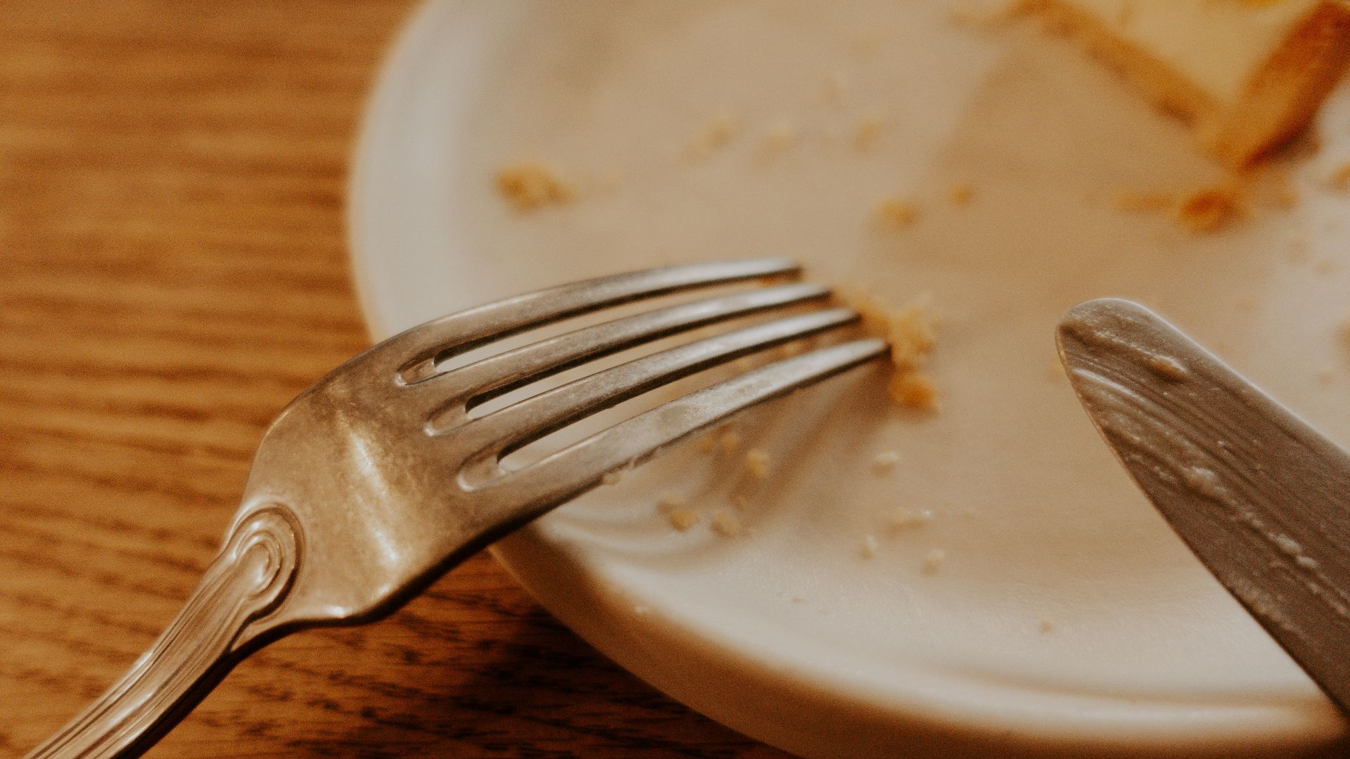 A close-up shot of a fork and knife on a plate with food remnants on a wooden table.