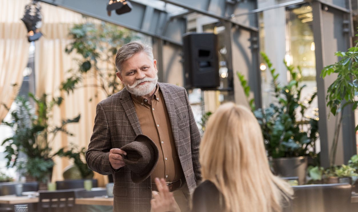 selective focus of smiling senior man with hat looking at woman at table in restaurant