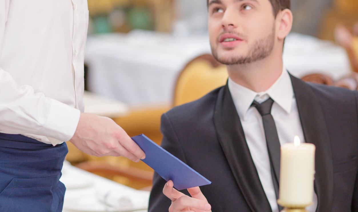 Receiving a bill. Handsome waiter giving a bill to his customer having dinner in the luxury restaurant 