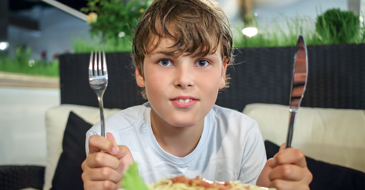 Boy with a knife and fork in front of a plate of pasta 